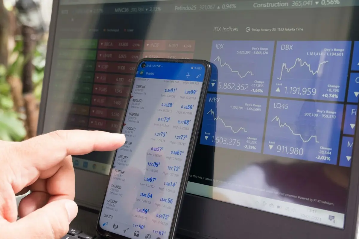 A finger pointing at currency quotes on a phone in front of a laptop