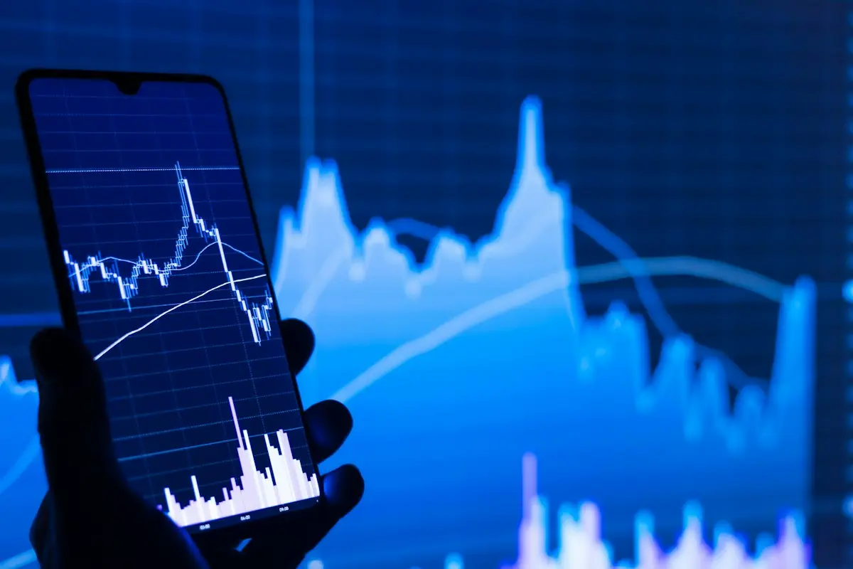 A phone showing a stock chart in front of a larger chart