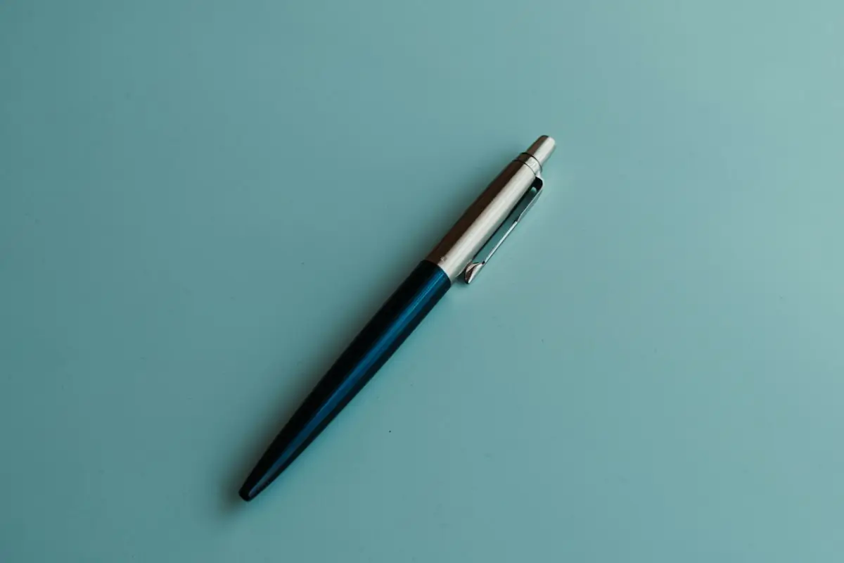A pen resting on a plain teal desk