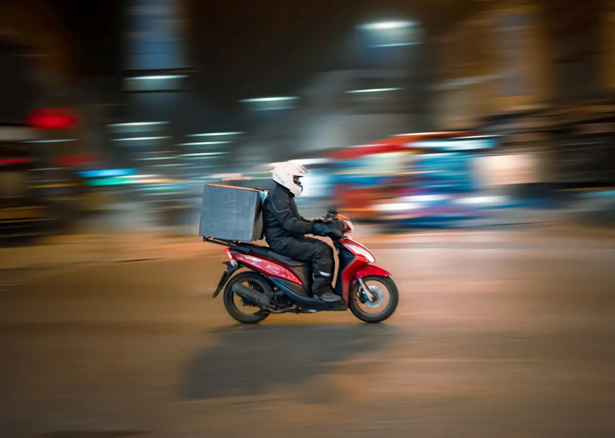 A delivery rider on a red scooter speeding through the city at night