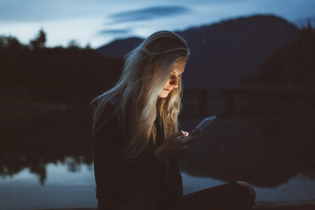 A woman checking her phone by a lake at dusk