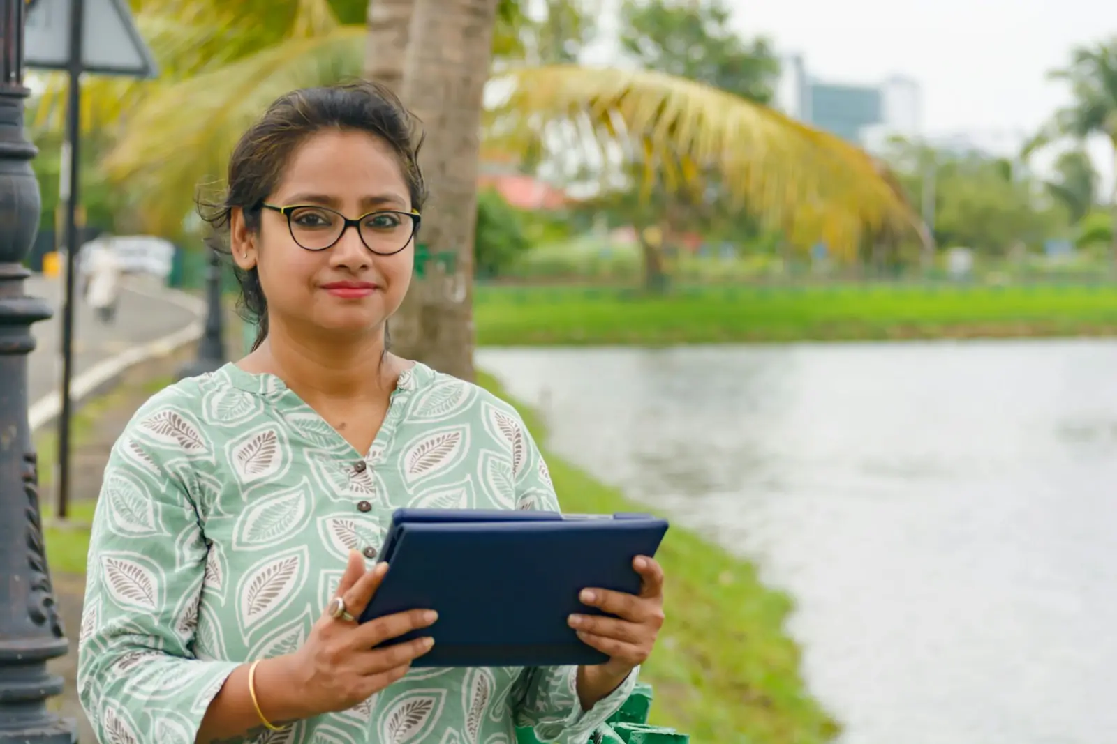 A woman in India holding a tablet by a lake