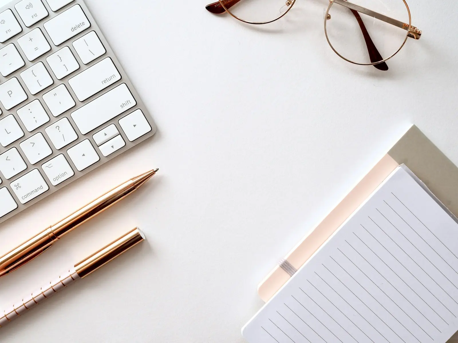 A keyboard, notebook and glasses on a white desk