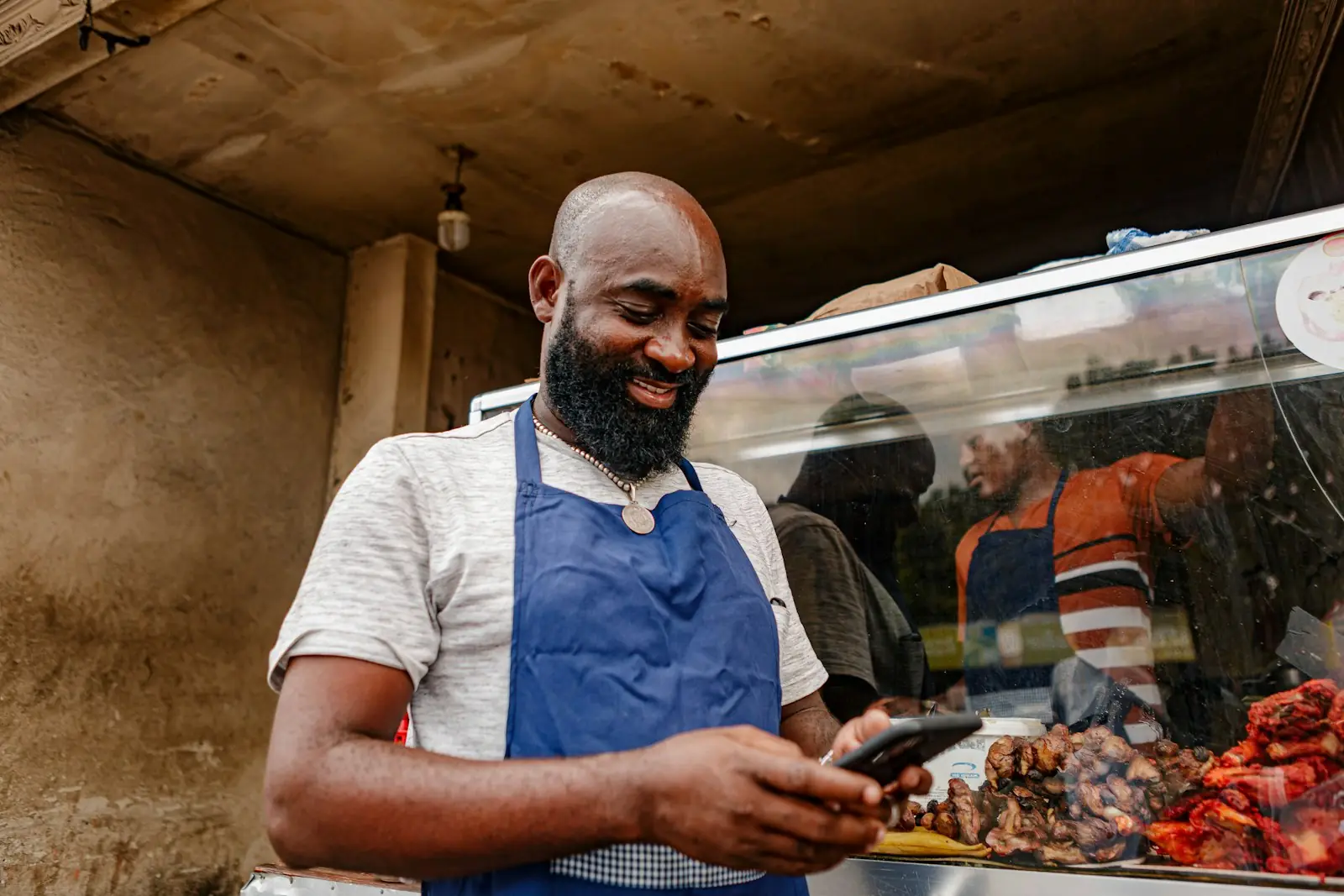 A shop owner in an apron checking his phone at the counter