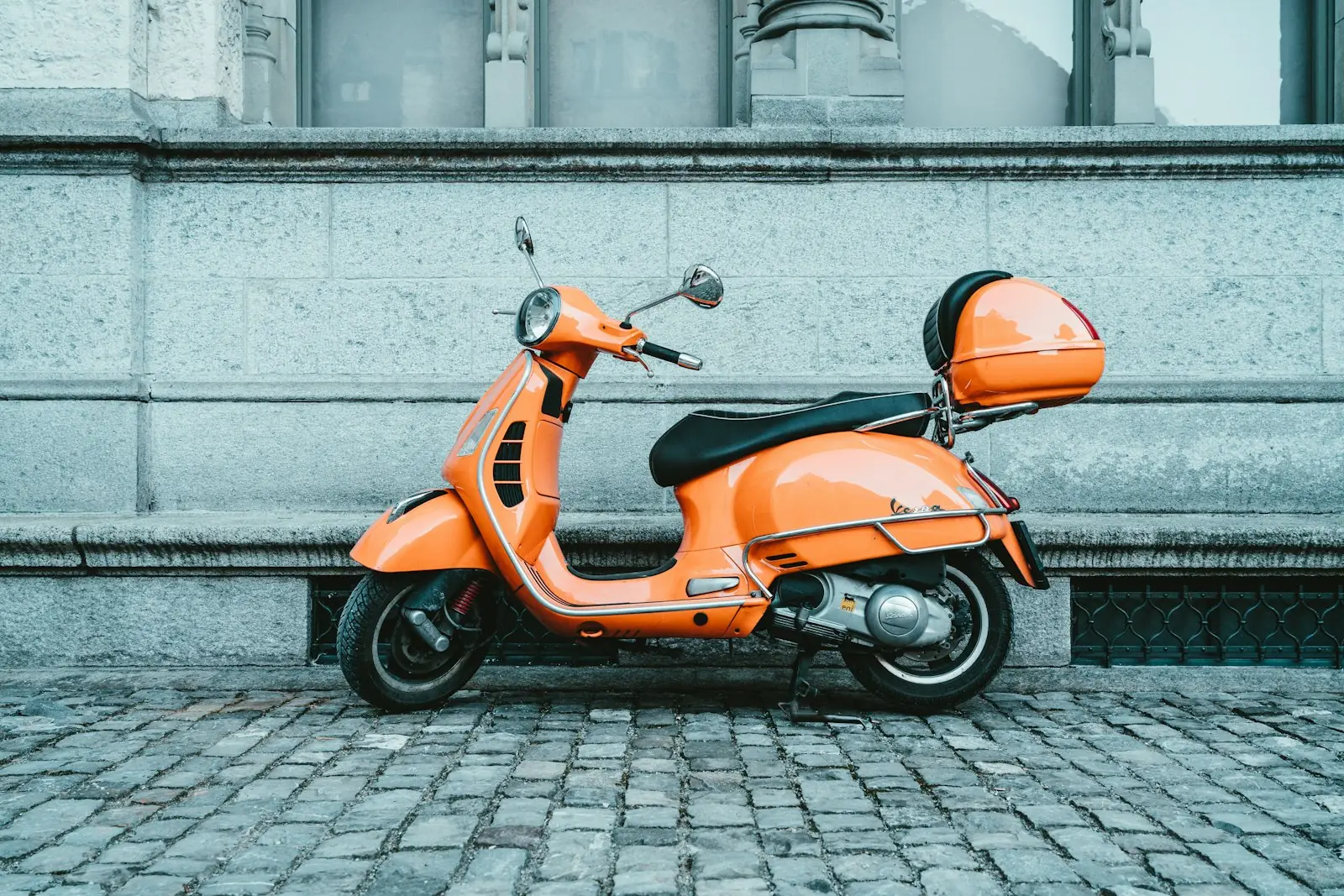 An orange motor scooter parked on a cobbled street